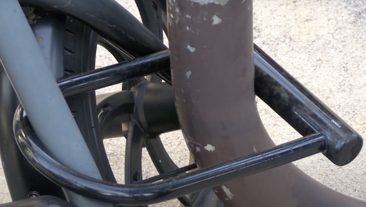 A black metal U-lock secures a bicycle to a brown metal bike rack